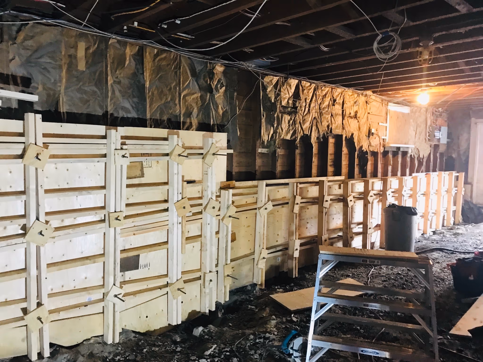 Wooden concrete forms line a basement wall during renovation, with exposed insulation and wiring.